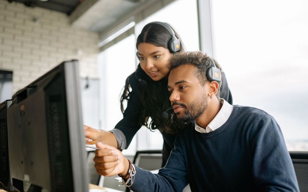 A colleague helping another resolve an issue at a monitor
